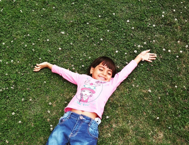 Young male child in pink shirt and jeans laying on grass with arms outstretched, smiling