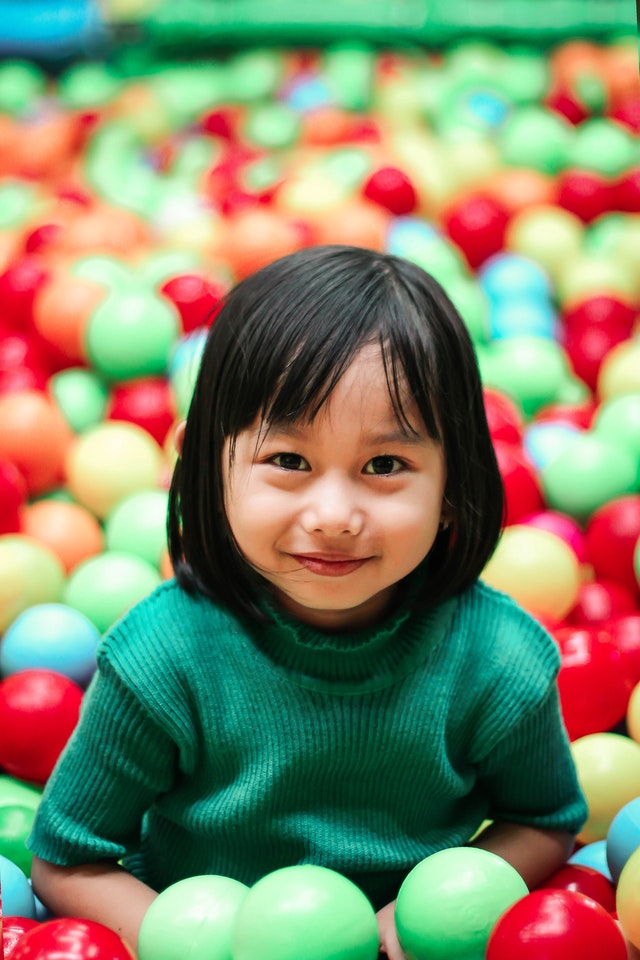 Young female child in ball pit wearing green sweater and smiling