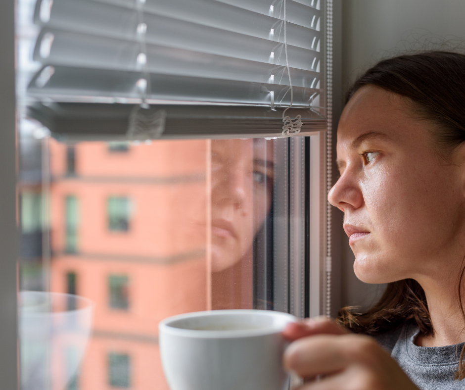 Anxious woman holding cup of coffee looking out apartment window
