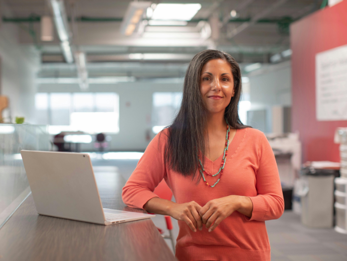 Smiling woman facing camera and using laptop in office setting