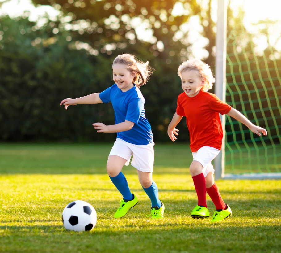 Two young, smiling children playing soccer outdoors